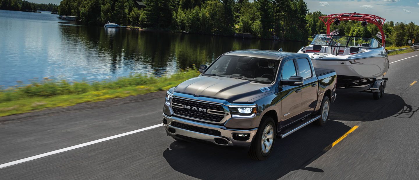 The 2023 Ram 1500 towing a motorboat beside a lake.