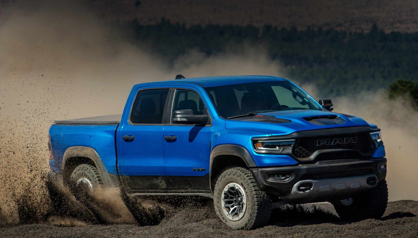 The 2023 Ram 1500 TRX being driven off-road on sand with a large cloud of dust obscuring its wheels.