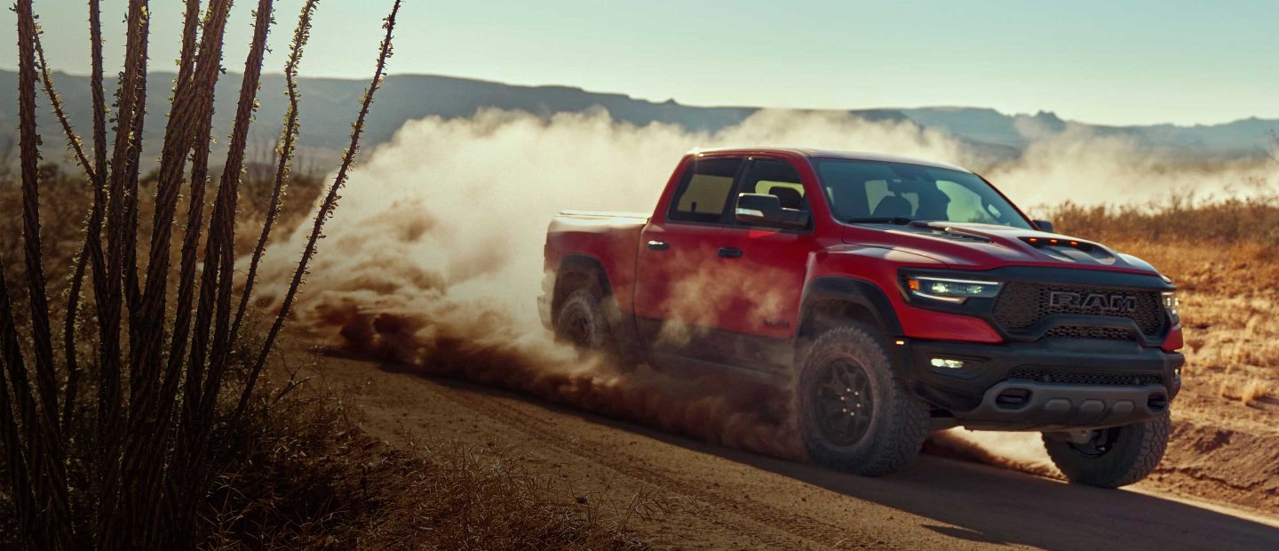 The 2023 Ram 1500 TRX being driven off-road in the desert on a dirt road with dust rising from its wheels.