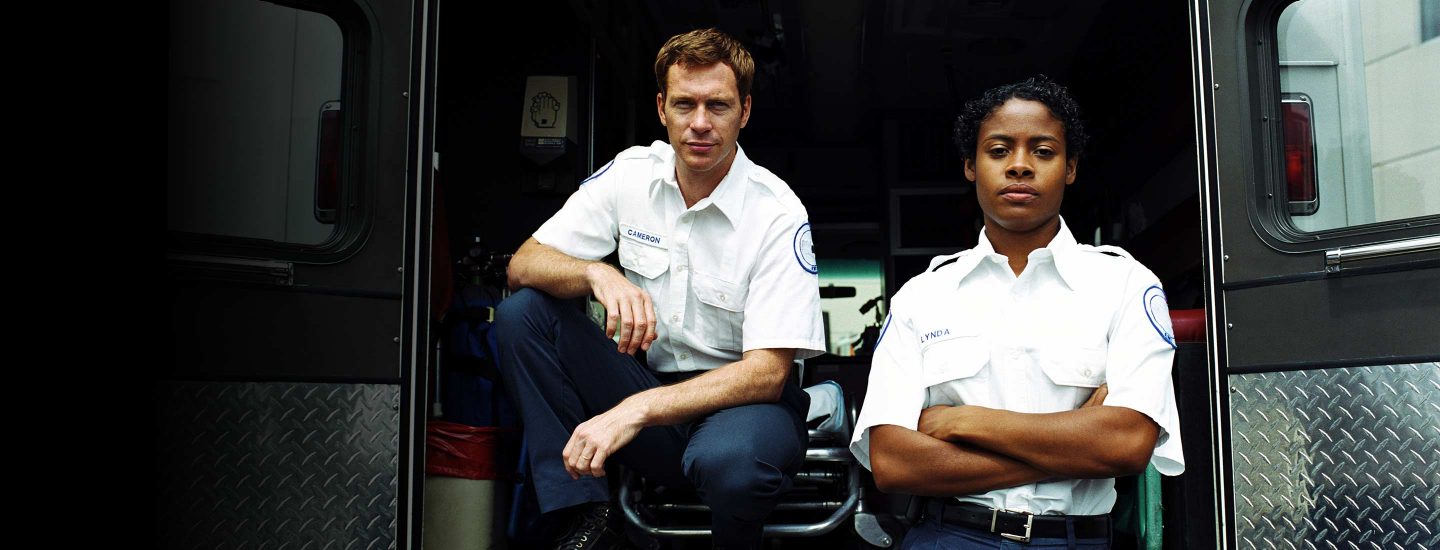 Two EMTs at the rear of an ambulance with its doors open.