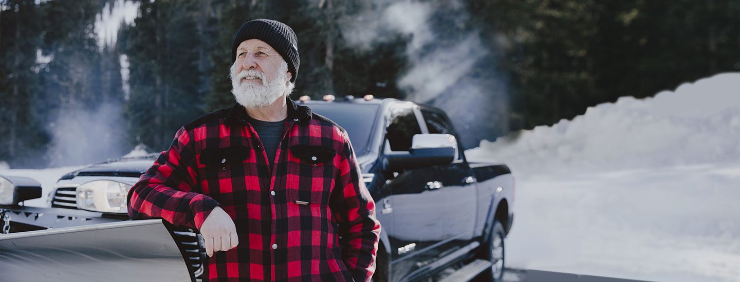 Vic Manson standing next to the hood of the 2020 Ram 2500 Laramie Crew Cab with a large stainless steel V-style plow attachment, and the North Shore Mountains in the background.