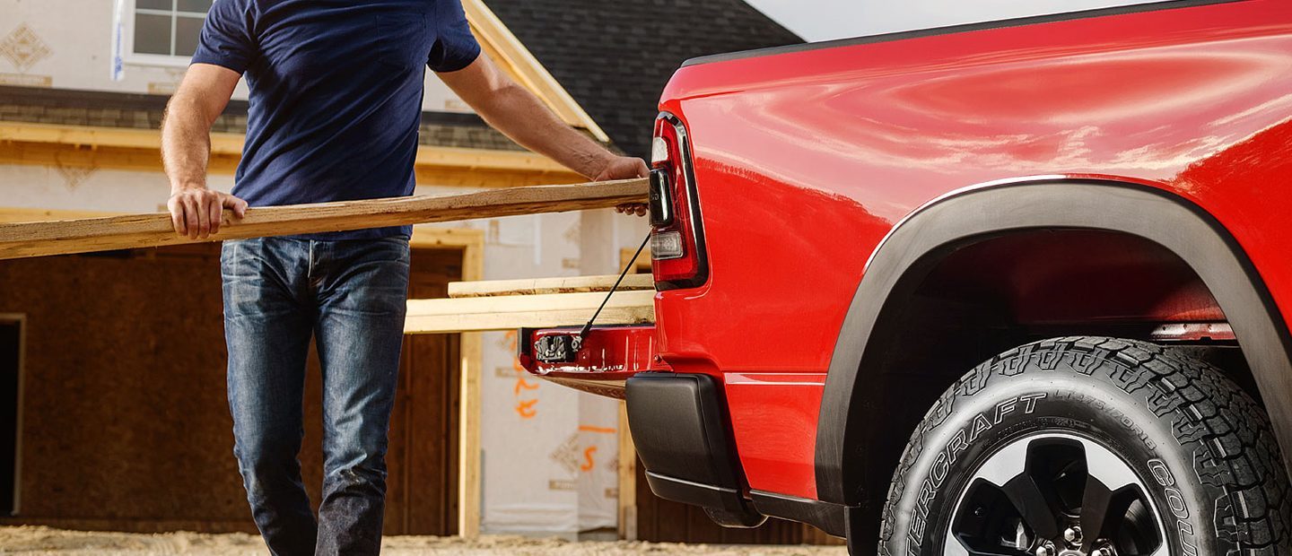 Two men loading a cooler into the bed of the 2023 Ram 1500 through the open doors of the multifunction tailgate.