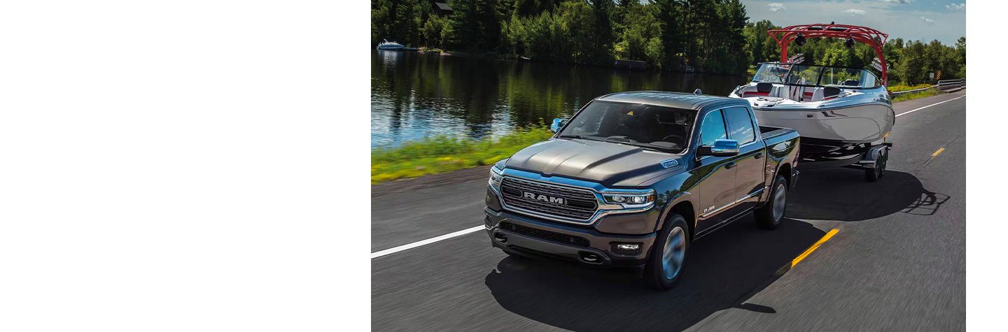 The 2023 Ram 1500 towing a motorboat beside a lake.